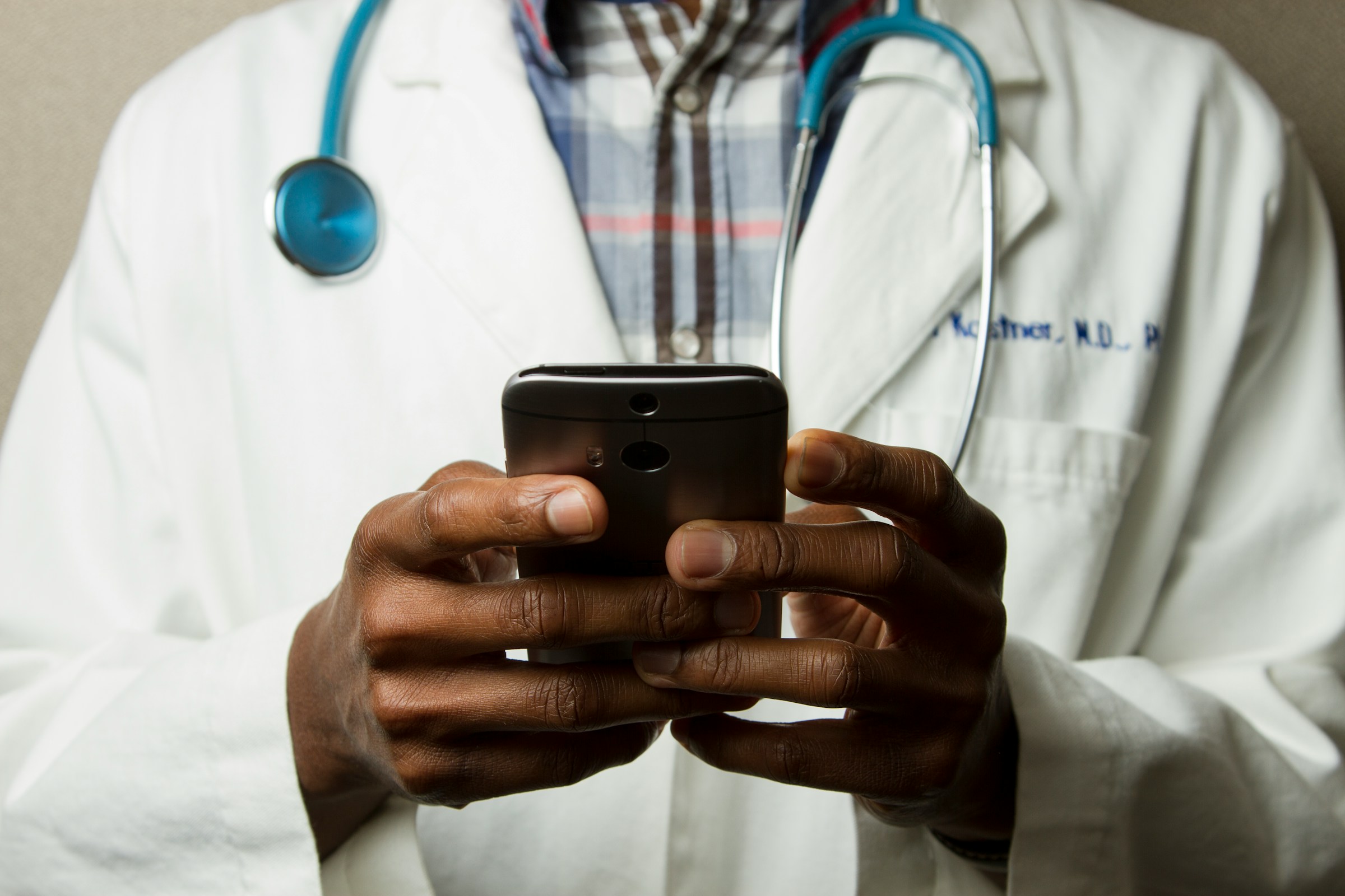 Doctor Holding Cell Phone. Cell phones and other kinds of mobile devices and communications technologies are of increasing importance in the delivery of health care. Photographer Daniel Sone. Photo by National Cancer Institute on Unsplash